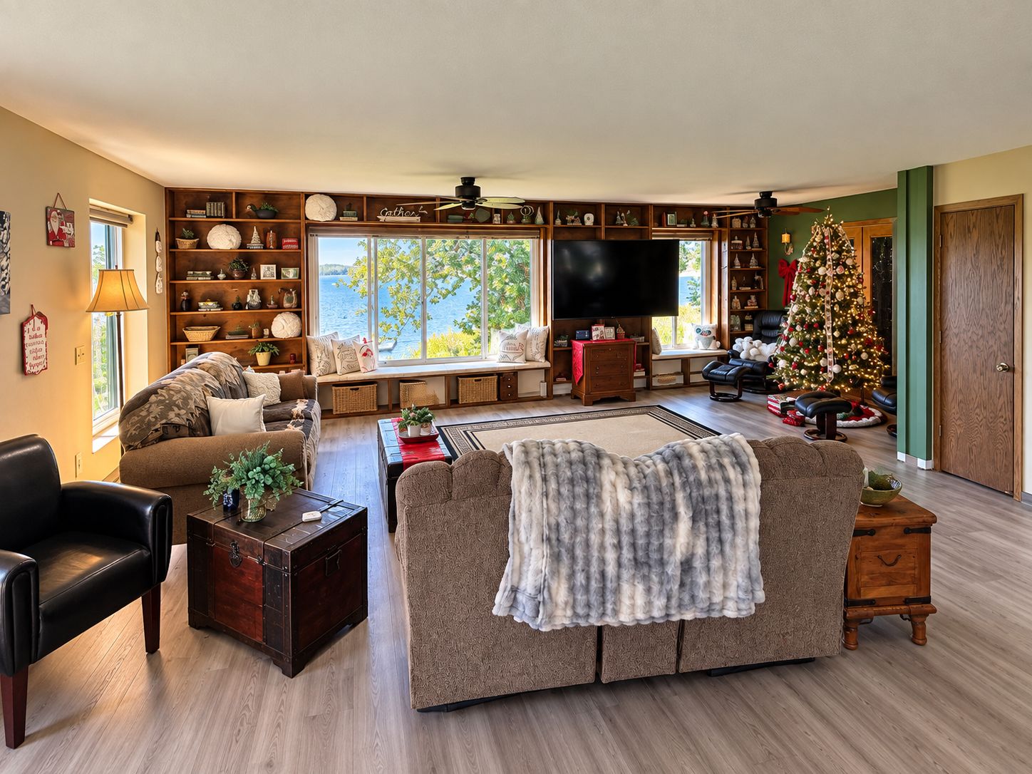 A cozy living room with a large window, a fireplace, a television, and a Christmas tree.