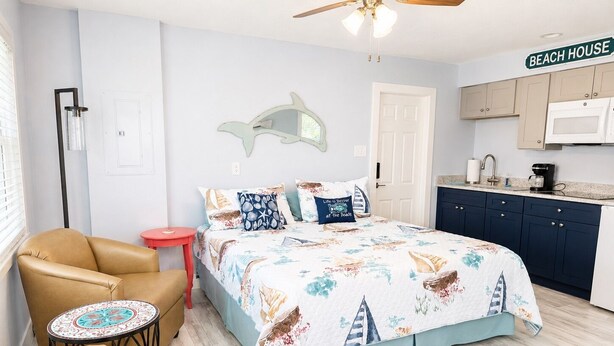 A bedroom with a bed, a chair, a small table, a kitchen area, and a ceiling fan. - Sweet SUITE on St. Pete Beach -- Perfect for your Beach Getaway (St. Pete Beach)