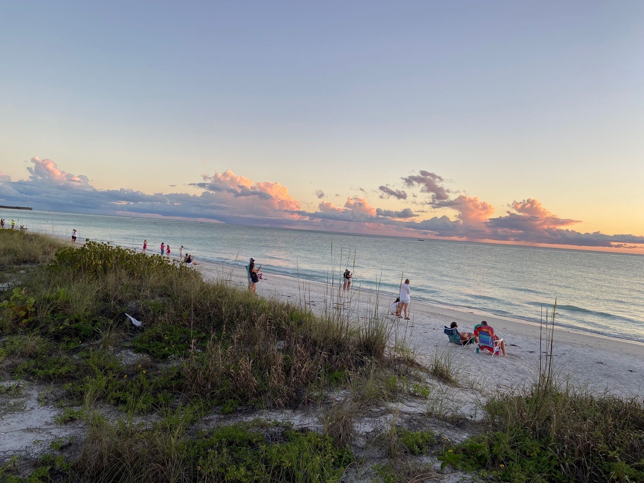A beach with people walking and sitting, and a boat in the distance.