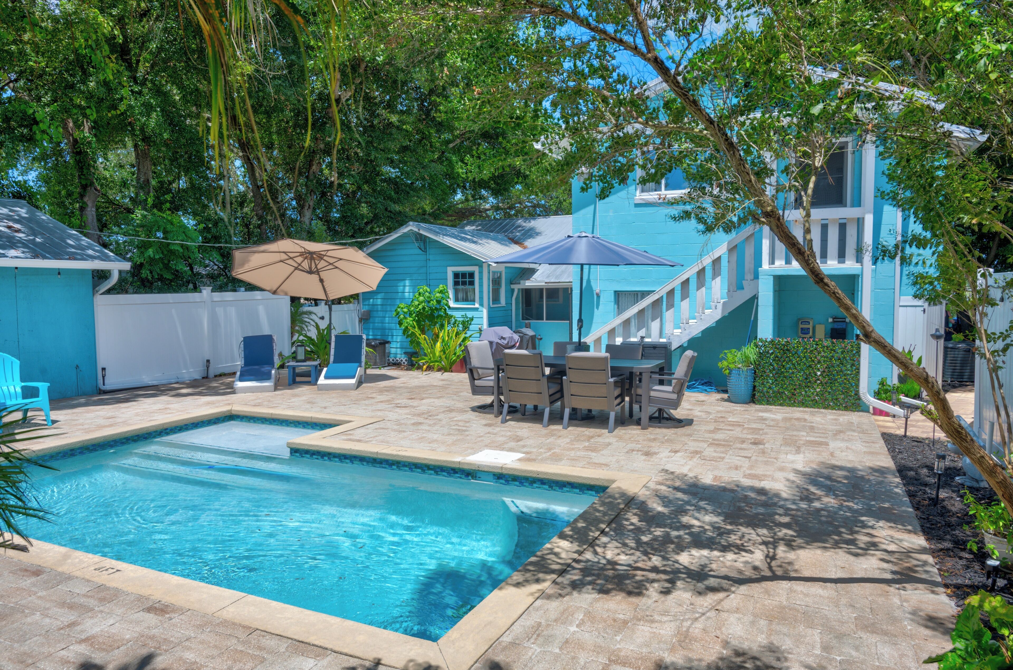 Un jardin avec une piscine, du mobilier d’extérieur et une maison bleue.