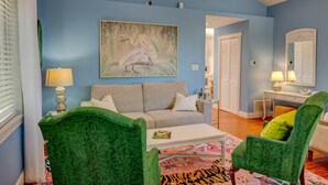 A living room with a blue wall, a painting of a bird, a sofa, a coffee table, and two green armchairs. - Hidden Gem: Private 650sq ft Studio, Free Parking, Pool, Walkable, Near Downtown (St. Augustine)