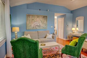 A living room with a blue wall, a painting of a bird, a sofa, a coffee table, and two green armchairs. - Hidden Gem: Private 650sq ft Studio, Free Parking, Pool, Walkable, Near Downtown (St. Augustine)