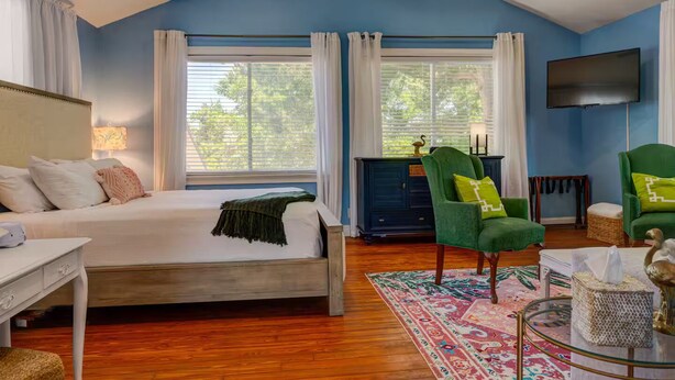 A bedroom with a bed, two green chairs, a TV, and a fireplace. - Hidden Gem: Private 650sq ft Studio, Free Parking, Pool, Walkable, Near Downtown (St. Augustine)
