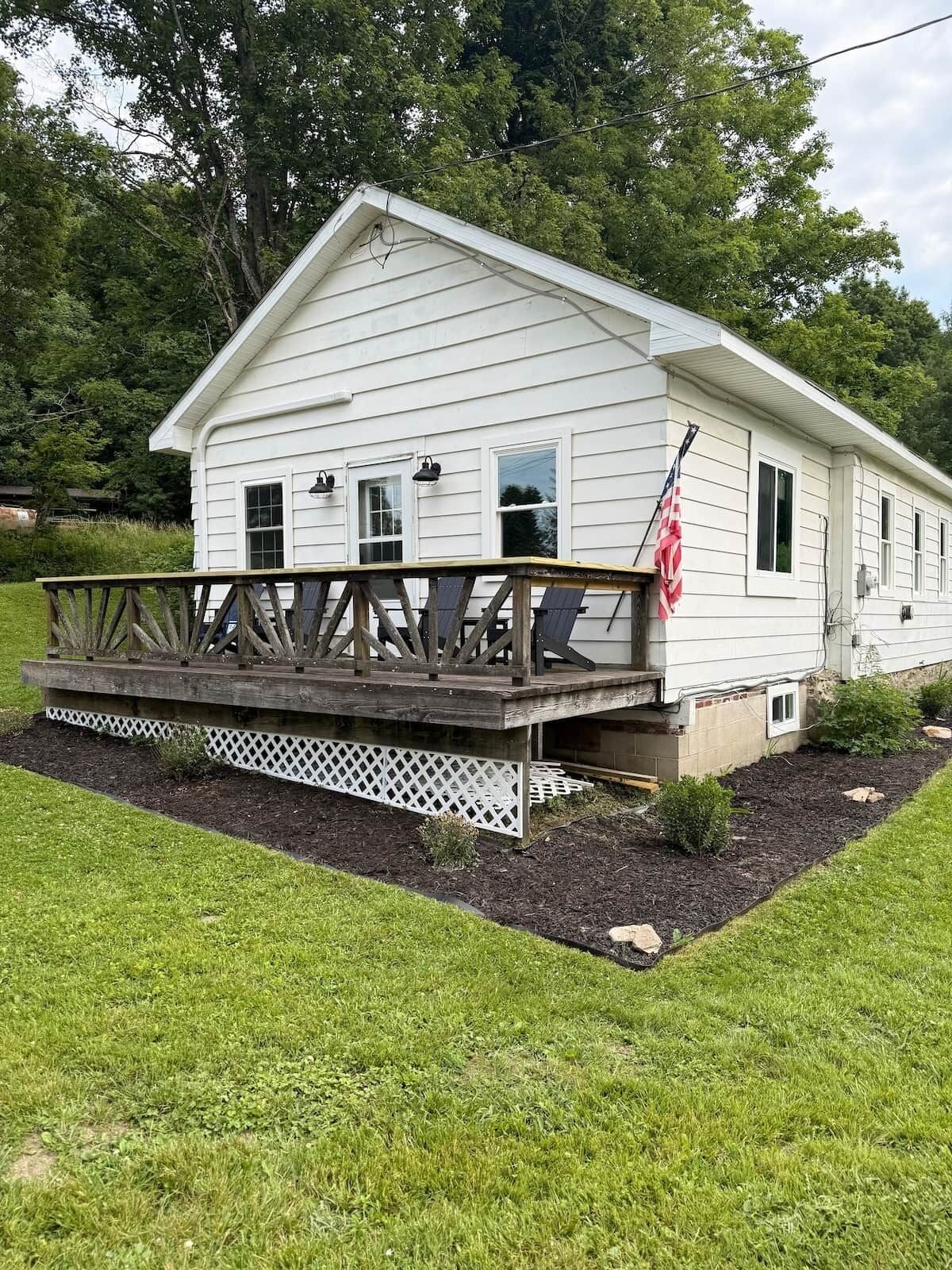 A white single-story house with a wooden deck and a small porch.