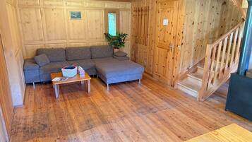 Een houten interieur met een bank, een bijzettafeltje, een trap en een plant.