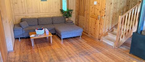 A wooden interior with a sofa, a small table, a staircase, and a plant.