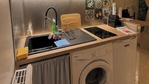 A compact kitchen with a built-in microwave, a sink with a faucet, a cutting board, and a washing machine. - Nice Studio "Azure Escape" (Nice)