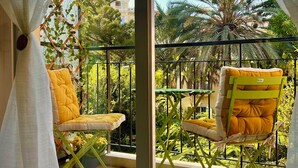 A balcony with two chairs, one yellow and one green, and a view of trees and buildings. - Nice Studio "Azure Escape" (Nice)