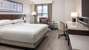 Habitación de hotel con una cama grande, un escritorio, una silla, un televisor y una ventana con cortinas.