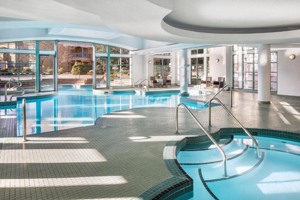 Ein großes Hallenbad mit großen Glaswänden, Fliesenboden und sonnendurchfluteter Innenausstattung.