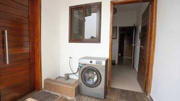 Ein Waschbereich mit Waschmaschine, einer Holztür und einem Spiegel an der Wand.