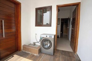 A laundry area with a washing machine, a wooden door, and a mirror on the wall. - Ina, votre beaux T2 lumineux avec piscine (Abidjan)