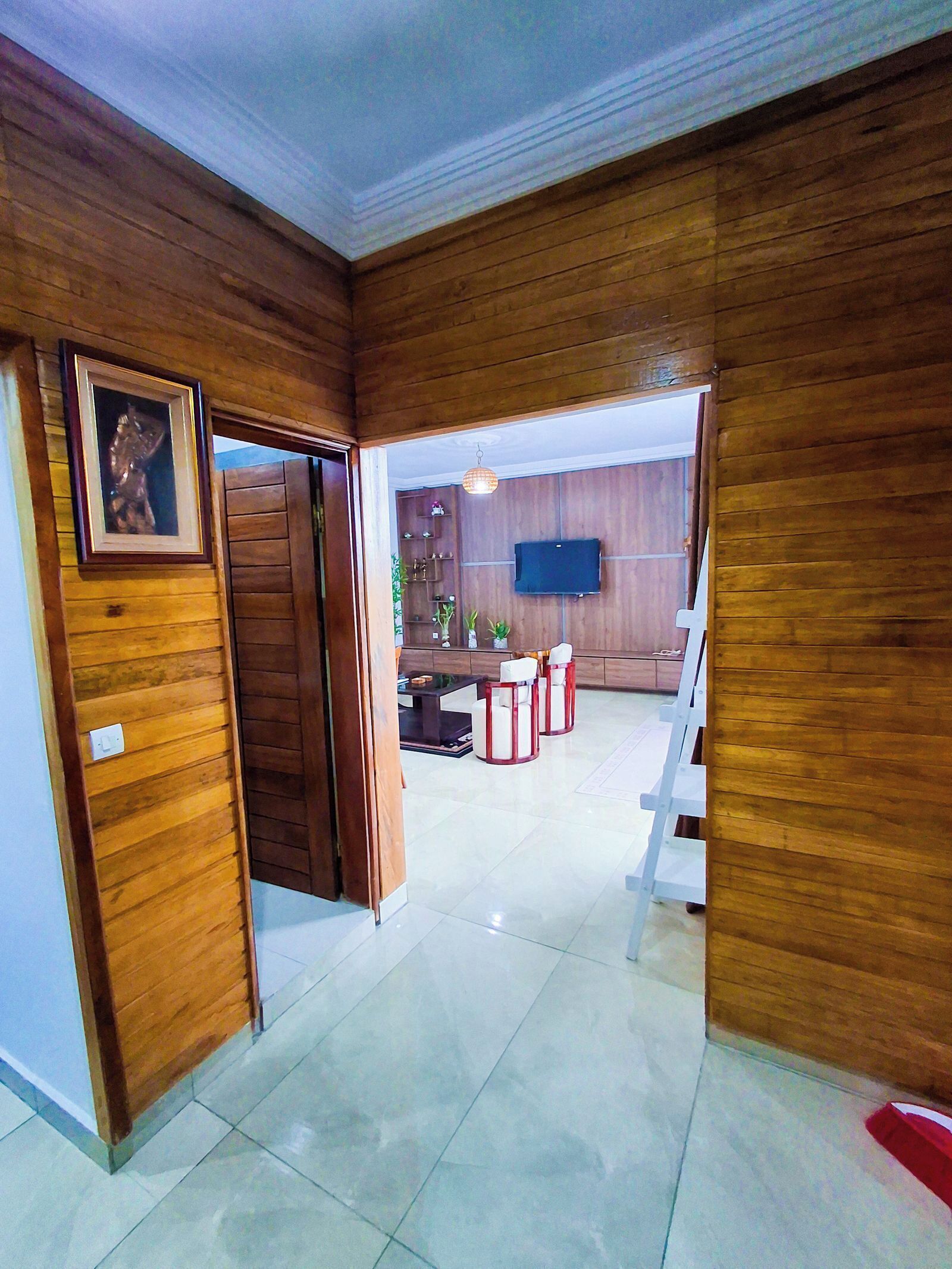 A room with wooden panel walls, a tiled floor, a desk with a chair, a television, and a hanging light fixture.