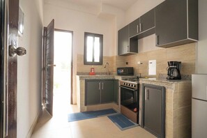A modern kitchen with dark cabinets, a microwave, a stove, and a refrigerator. - Ina, votre beaux T2 lumineux avec piscine (Abidjan)