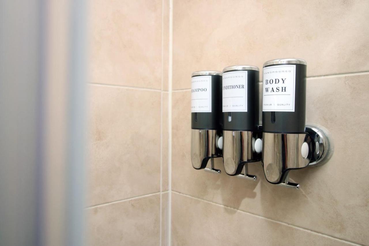Un distributeur mural doté de trois flacons étiquetés « Shampoing », « Après-shampoing » et « Gel douche ».