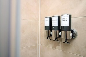 Un distributeur mural doté de trois flacons étiquetés « Shampoing », « Après-shampoing » et « Gel douche ».