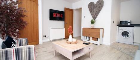 Un salón moderno con una mesa de centro de madera, un sofá, un televisor montado en la pared y una decoración con forma de corazón.