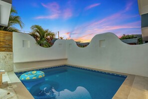A swimming pool with a wooden deck, surrounded by white walls and palm trees, under a clear sky. - Luxury Beach Villa | 1-Min Walk to Beach & Private Pool (paquera)