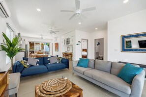 A modern living room with two sofas, a coffee table, ceiling fans, and a dining area in the background. - Luxury Beach Villa | 1-Min Walk to Beach & Private Pool (paquera)