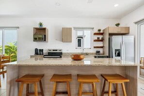 Eine moderne Küche mit einer zentralen Kochinsel, Holzbarhocker, einem Einbauofen und einem Kühlschrank.