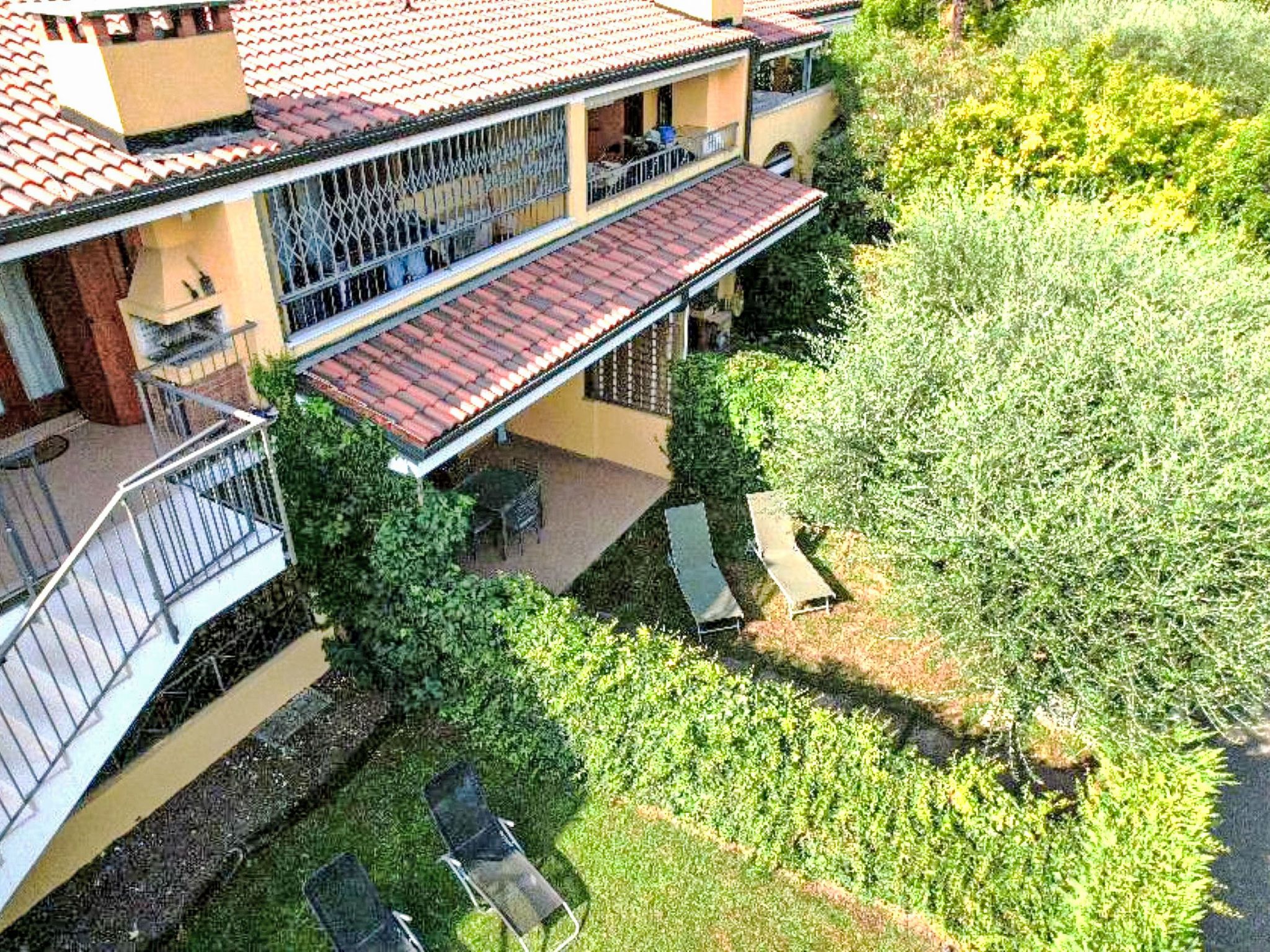 A two-story building with a red-tiled roof, a balcony, and a garden area with a table and chairs.