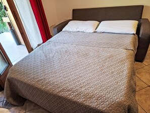 A bed with a quilted cover, a headboard, and a window with curtains. - Apartment  by Interhome (Lazise)