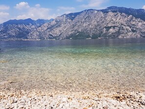 A clear lake with a rocky shore and mountains in the background. - Apartment  by Interhome (Lazise)