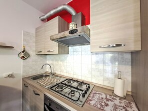 A kitchen with a gas stove, stainless steel sink, and wooden cabinets. - Apartment  by Interhome (Lazise)