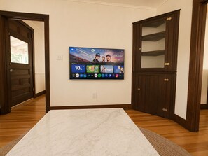 A room with a large flat-screen TV mounted on the wall, a wooden door, and a marble floor. - Camp Coronado- Classic Summer House in the Village of Jamestown (Jamestown)