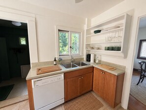 A compact kitchen with a dishwasher, wooden cabinets, a sink, and a window. - Camp Coronado- Classic Summer House in the Village of Jamestown (Jamestown)