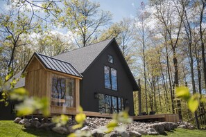 A cabin with a large window, a wooden deck, and a stone foundation. - New Luxury Lakeside Cabin with Sauna & Cedar Hot Tub - The Narrows (Pillager)