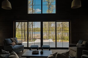 Ein modernes Wohnzimmer mit großem Fenster, Blick auf Wald und See.