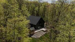 Eine Holzhütte, umgeben von dichtem Wald, mit freiem Blick auf die Bäume und einem Kiesweg, der zum Eingang führt.