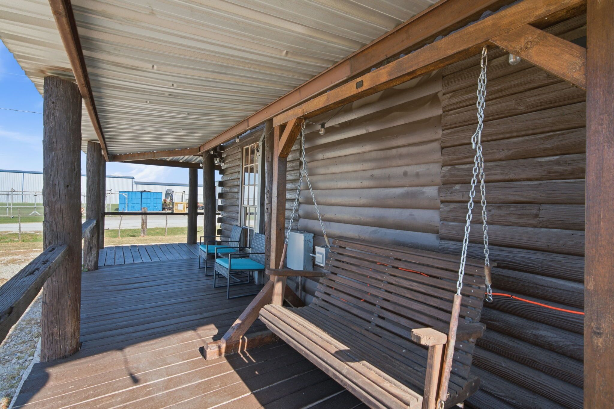 A covered wooden deck with a bench and a table, overlooking an industrial area.
