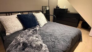 Un dormitorio con cama, una manta suave, un escritorio y una lámpara.