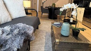 Una sala de estar moderna con un sofá, una mesa de centro con objetos decorativos, una escalera y una zona de cocina.