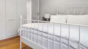 Une chambre à coucher avec un lit en métal blanc, une armoire blanche et une table de chevet avec une lampe.