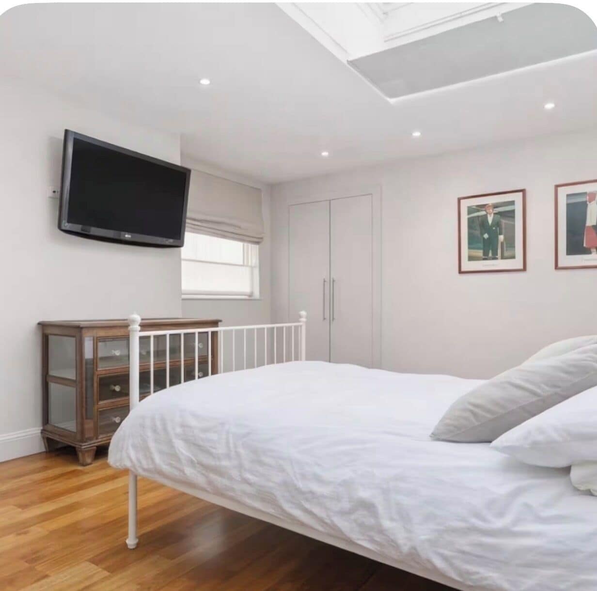 A bedroom with a bed, a television mounted on the wall, a wardrobe, and a window with curtains.