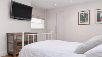 A bedroom with a bed, a television mounted on the wall, a wardrobe, and a window with curtains.