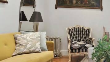 A living room with a yellow sofa, a patterned armchair, a glass coffee table, and a painting on the wall.
