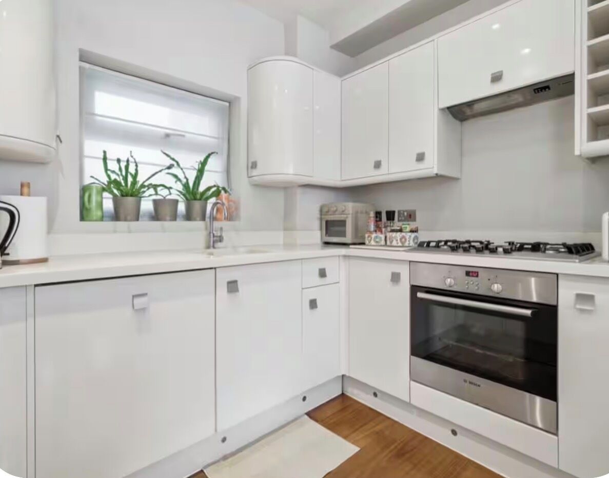 Una cucina moderna con mobili bianchi, forno integrato e una finestra con piante in vaso.
