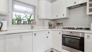 Une cuisine moderne avec des meubles blancs, un four encastré et une fenêtre agrémentée de plantes en pot.