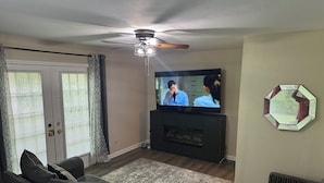 Un soggiorno con divano, televisore, ventilatore a soffitto e un elemento decorativo a parete.