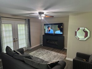 A living room with a sofa, television, ceiling fan, and a decorative wall piece.