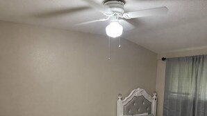 Quarto com duas camas, ventilador de teto e janela com cortinas.