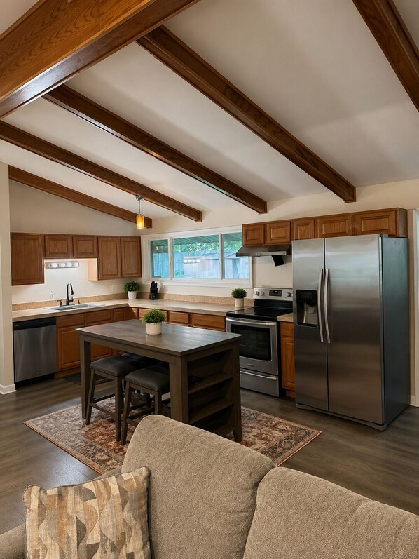 A modern kitchen with wooden cabinets, a stainless steel refrigerator, and a dining area with a table and chairs.