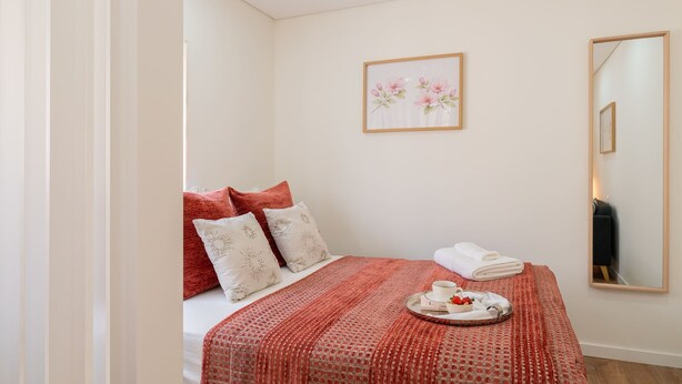 A hotel room with a bed, pillows, a tray with toiletries, a framed floral artwork, and a mirror. - 3 Apartments with Swimming Pool by HostWise (Moreira)