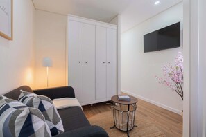 Quarto moderno com sofá, guarda-roupa, televisão e uma pequena mesa com um livro.