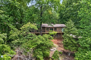 A secluded cabin surrounded by dense forest, with a visible deck and a dirt path leading to the entrance. - Sunset Cove — Lake Keowee Luxury Retreat with Private Dock + Hot Tub (Seneca)