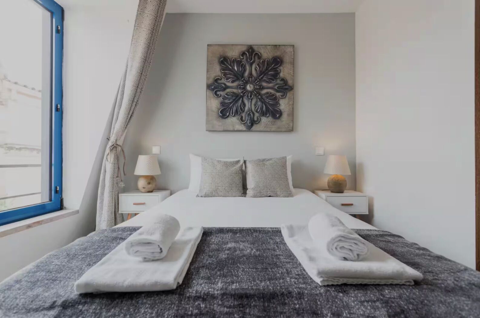 A neatly made bed with folded towels, a decorative wall piece, and two bedside lamps.